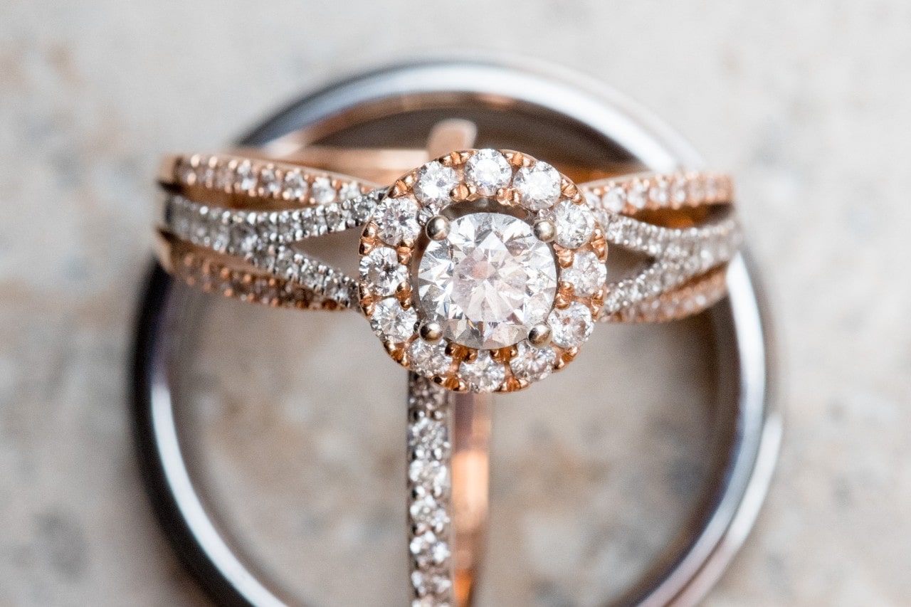 A close-up of an opulent halo engagement ring, displayed alongside two wedding bands.