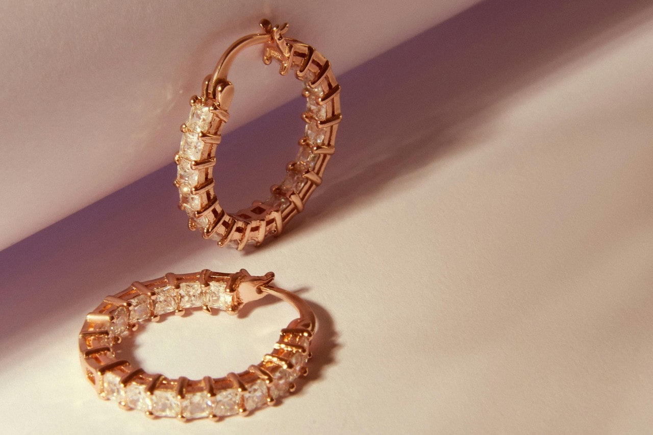 a pair of yellow gold diamond huggies earrings on a beige surface