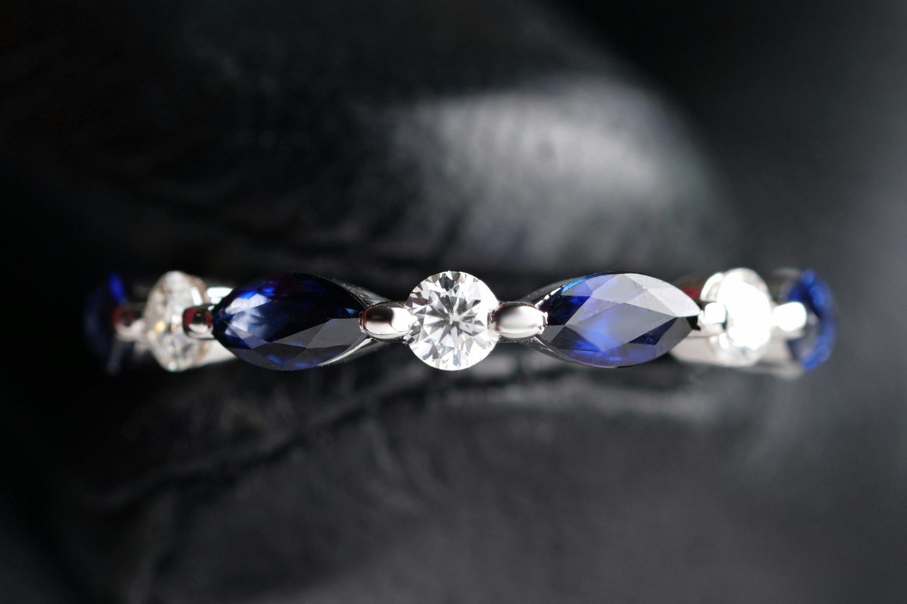 A detailed shot of a silver band adorned with alternating marquise-cut blue sapphires and round-cut diamonds on a black surface.