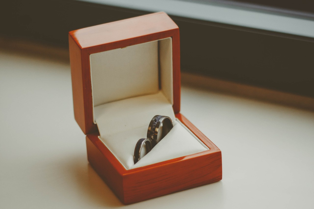 A pair of matching wedding bands with black diamonds in a red wooden jewelry box
