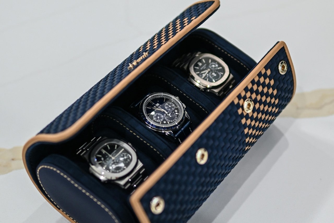Three luxury watches showcased in an open blue-and-tan checkered display case.