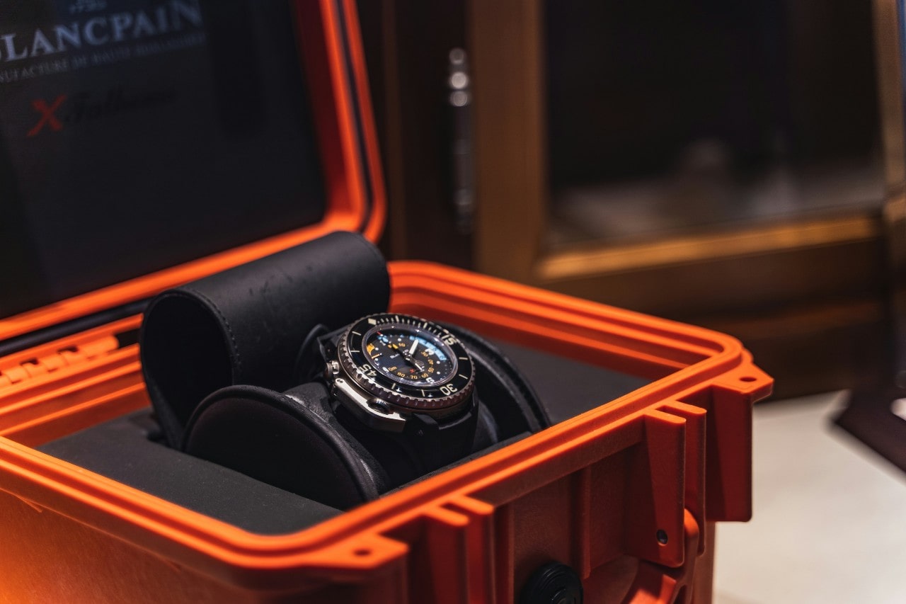 Luxury dive watch with luminous markers set in a sturdy, orange protective case.