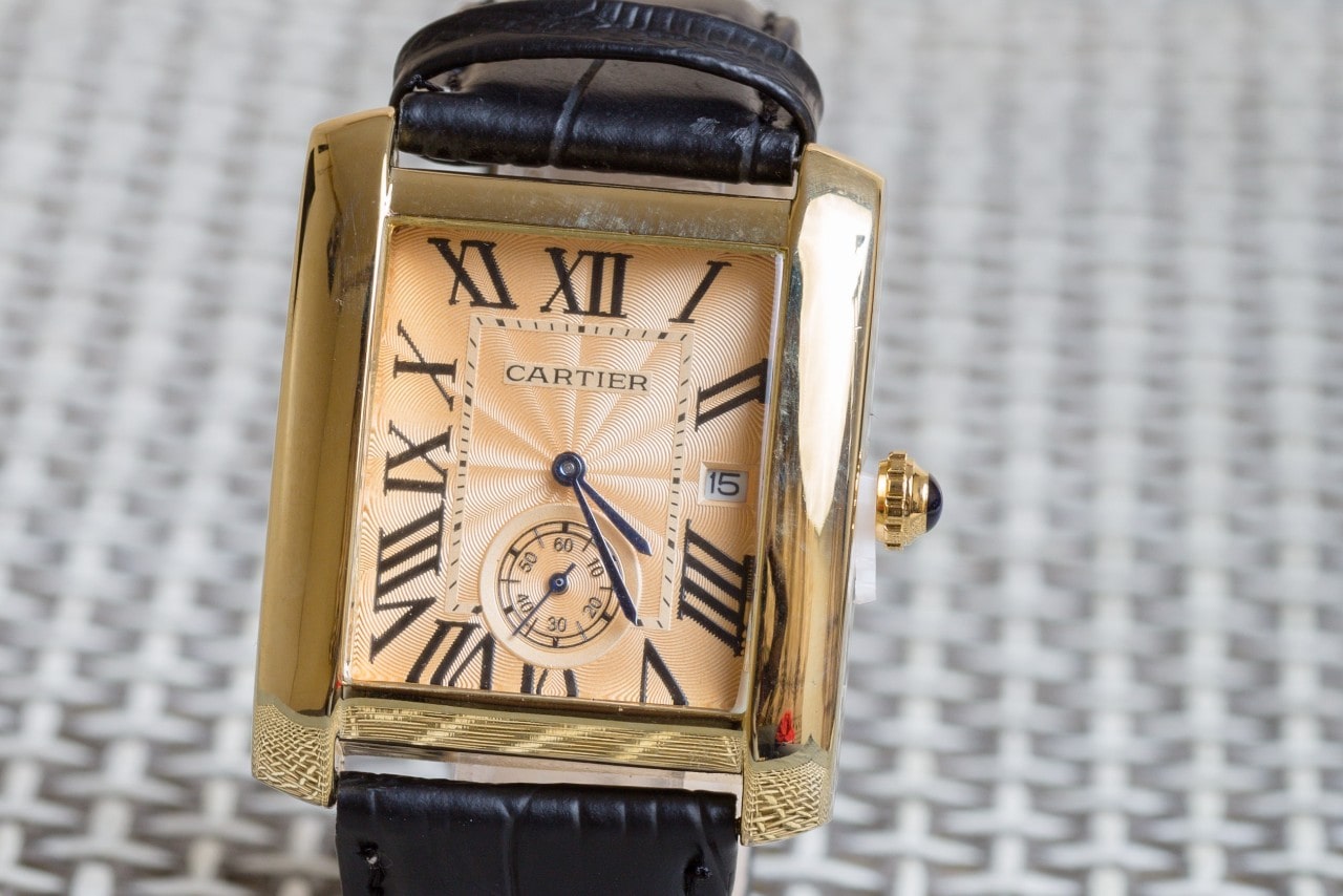 A close up of leather Cartier wristwatch with orange dial and yellow gold square bezel