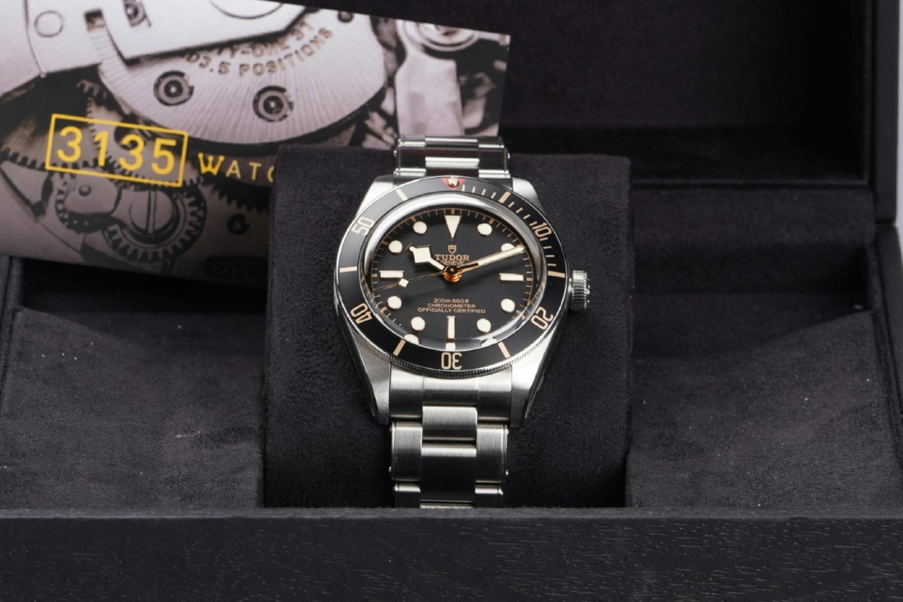 A luxury wristwatch with a black bezel and stainless steel bracelet rests in a black velvet box.