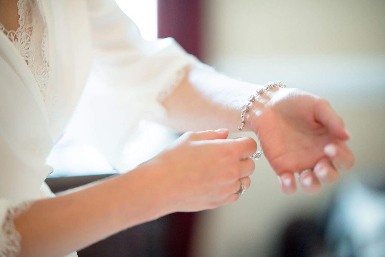 A woman in a white lace-trimmed robe is delicately clasping a silver bracelet on their wrist.