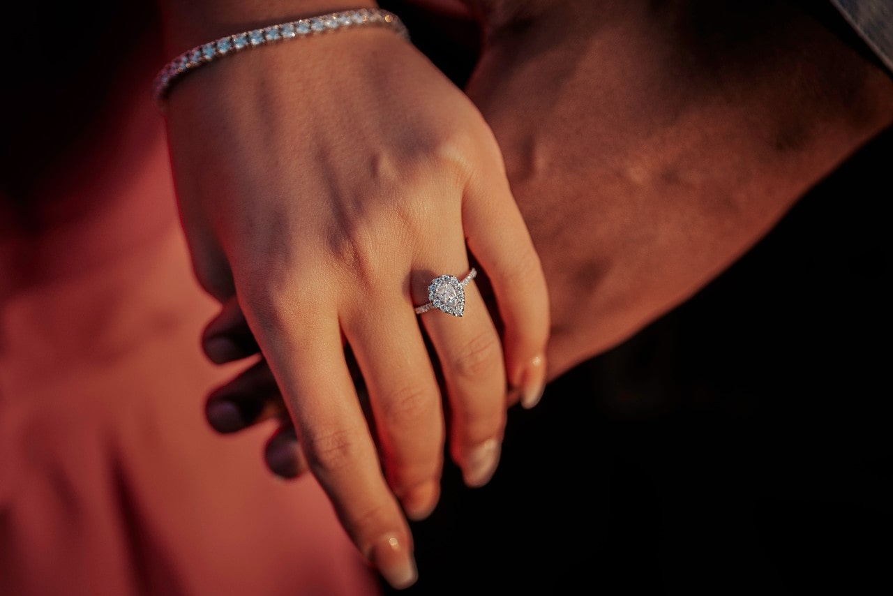 Close-up of the couple's hands, highlighting a pear shaped diamond ring.