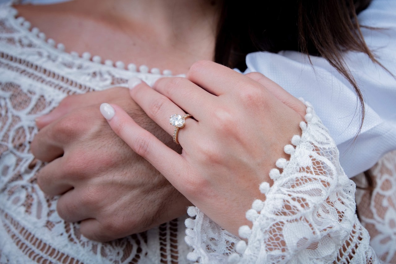 Close-up of a woman's hand with a solitaire engagement ring resting on a man's hand.