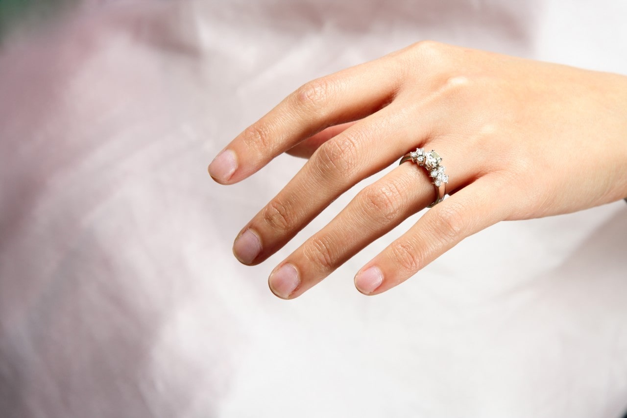 Close up of a hand adorned with a three stone diamond engagement ring