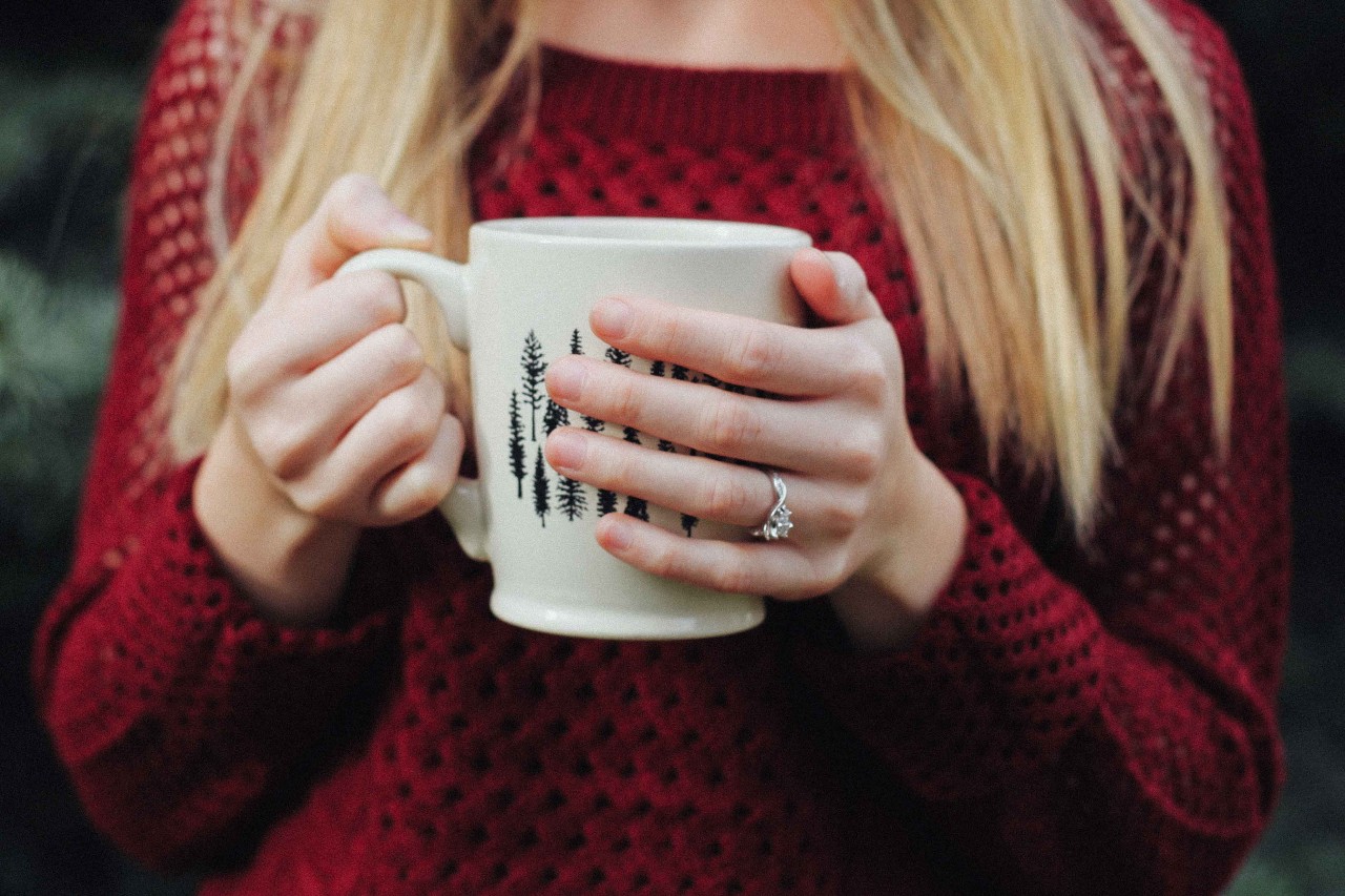 A woman in a sweater sips coffee out of a mug, wearing a twisted shank ring. A woman in a sweater sips coffee out of a mug, wearing a twisted shank ring.