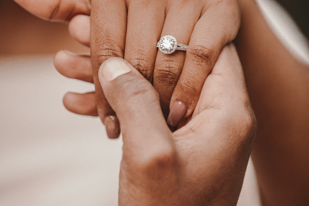 A woman wearing a split shank halo engagement ring holds a man’s hand. A woman wearing a split shank halo engagement ring holds a man’s hand.