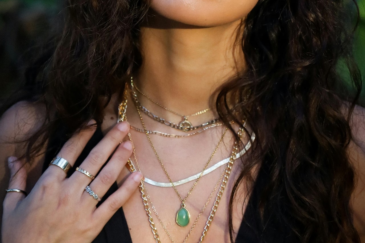 a woman’s neckline adorned with layered necklaces and wearing layered fashion rings