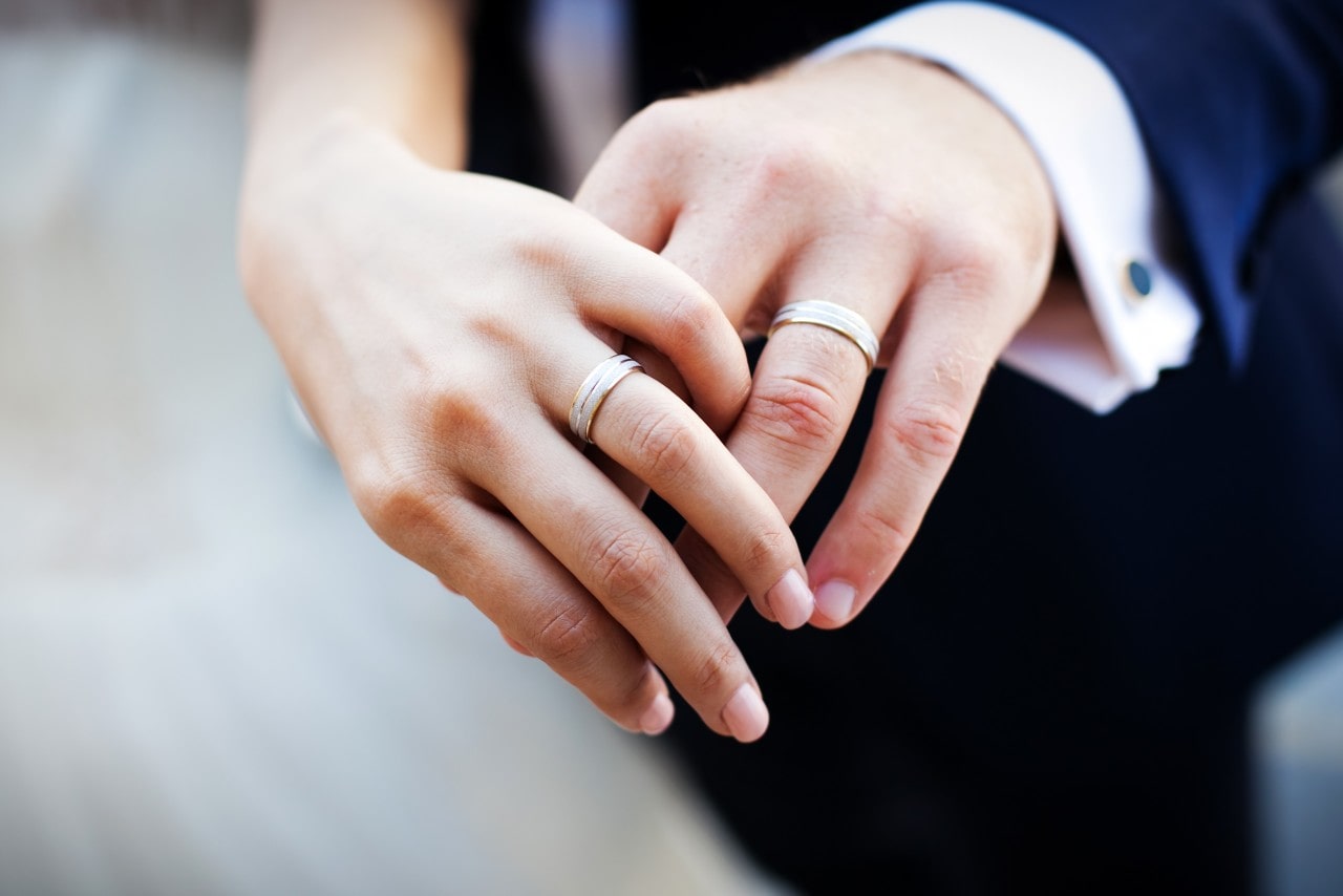 A pair of intertwined hands wearing matching white gold wedding bands, highlighting the couple's rings. A pair of intertwined hands wearing matching white gold wedding bands, highlighting the couple's rings.