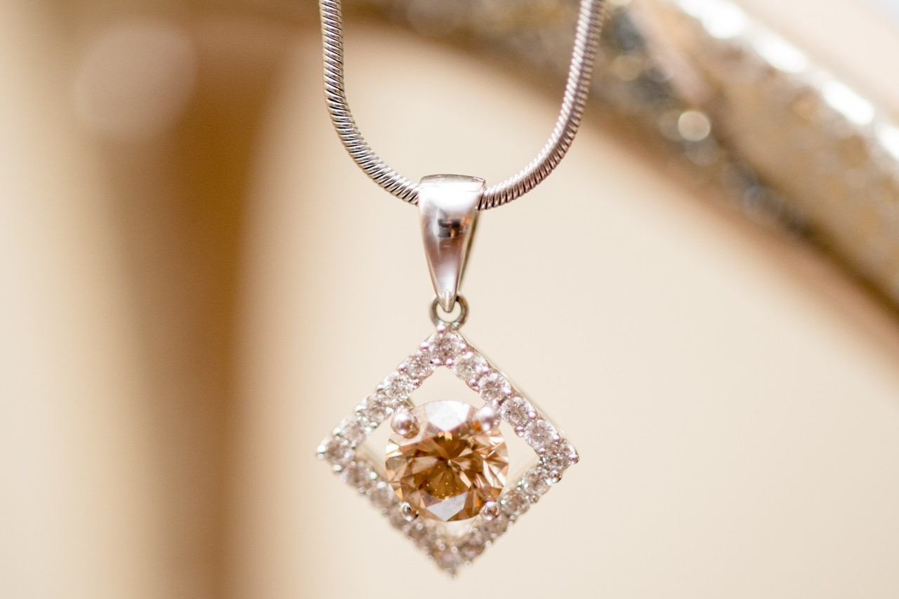A close-up of a diamond necklace, an amber-colored circular stone with a diamond shaped halo of diamonds holding it.