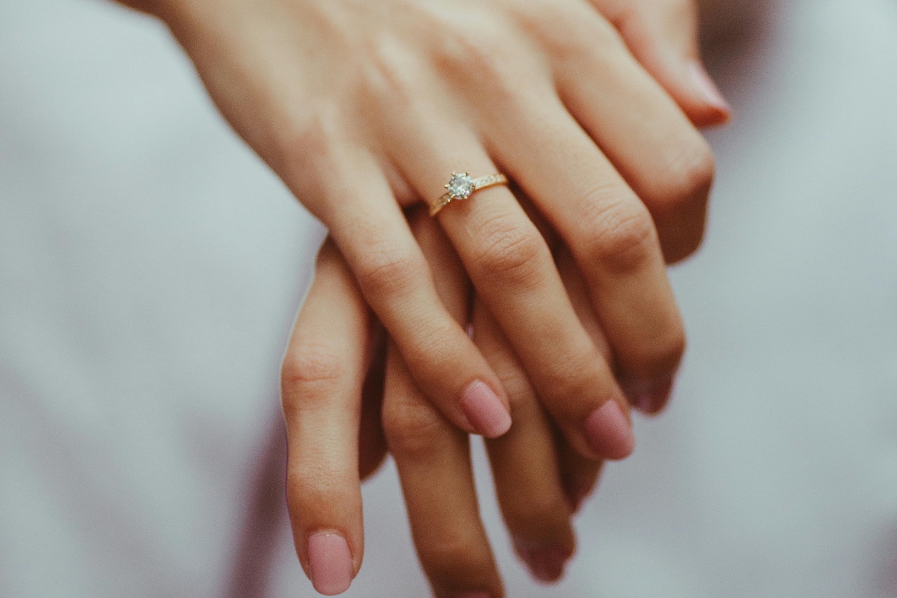 Close up of hands, adorned with a round cut diamond engagement ring.