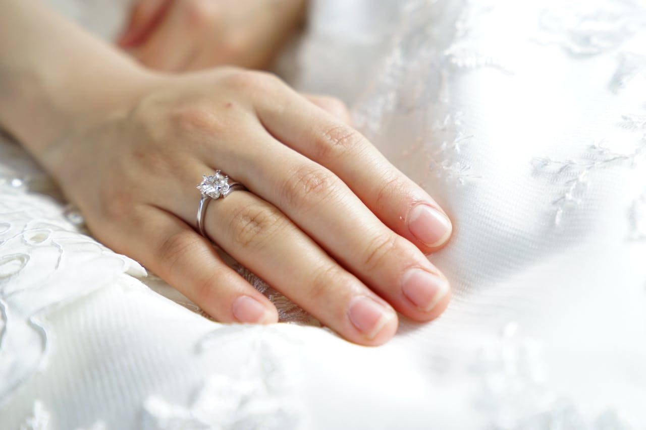 A close up of a woman’s hand on a white embroidered fabric with white gold diamond engagement ring.